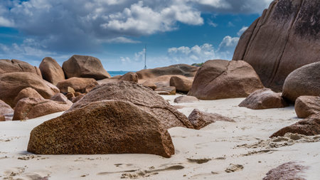 Weathered granite boulders are piled on a tropical beach. Footprints in the sand. Turquoise ocean in the distance. The yacht's mast is visible against the background of the skyの写真素材