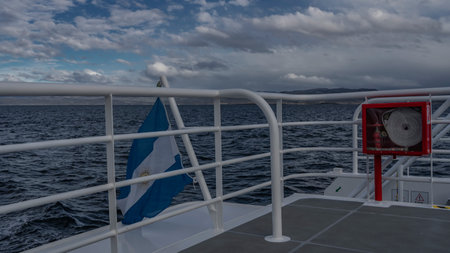 The side of the yacht is fenced with metal railings. The blue and white flag of Argentina is flying over the water. In the distance you can see the coast of Patagonia. blue sky,の写真素材