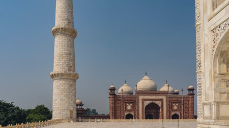 Details of the architecture of the Taj Mahal. A high white marble minaret and part of the wall with an arch and inlays of precious stones. Against the blue sky is the Kau Banの写真素材