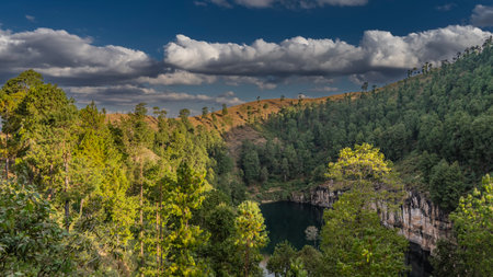 A beautiful lake in the crater of an extinct volcano is surrounded by steep rocky shores. Coniferous forest grows on the hills. picturesque clouds in the blue sky. Madagascar.の写真素材