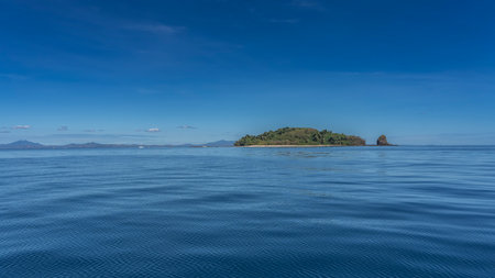 A green island is visible in the calm blue ocean. A mountain range on the horizon. Clear azure sky. Madagascar. Nosy Tanikeliの写真素材