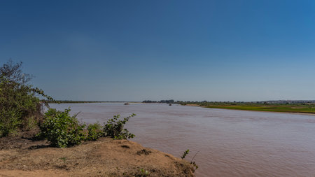 The red-brown river flows calmly. Ferries can be seen in the riverbed ferrying cars across the stream. Green vegetation on the banks. Clear blue sky. Copy space. Madagascar.の写真素材