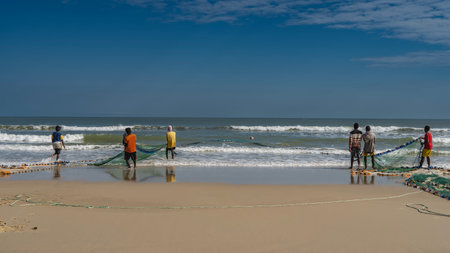 Fishermen pull a fishing net out of the ocean. Turquoise waves roll towards the shore, foaming. Reflection on wet smooth sand. Clear blue sky. Copy space. Madagascar. Morondava.の写真素材