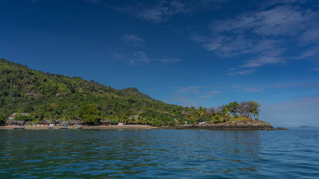 A picturesque tropical island against a background of blue sky and clouds. Lush green vegetation on the hill. Houses with thatched roofs near the shore. The boats are mooredの写真素材