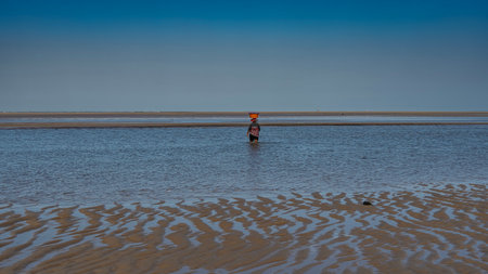 Low tide. Pools of water on the exposed undulating sandy seabed. A woman walks through shallow water...
