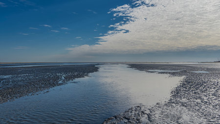 Low tide time. Streams flow to the ocean, puddles on the exposed wavy sandy seabed. Clouds and blue sky are reflected in the water. Madagascar. Morondava. The Mozambique Channel.の写真素材