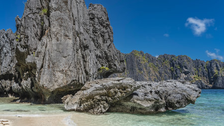 Beautiful karst rocks with bizarre outlines rise above the aquamarine lagoon. There is green vegetation on the gray steep slopes. Sandy beach. Clouds in the blue sky. Philippines.の写真素材