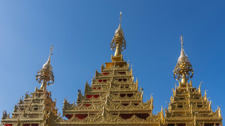 The spectacular roof of the temple against a clear blue sky. Pyramidal golden towers with openwork...
