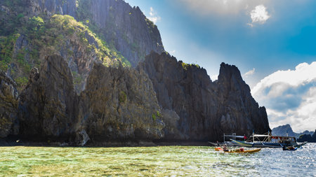 Traditional Filipino bangka boats are anchored in the bay. The canoe is floating. Steep coastal karst cliffs against a background of blue sky and clouds. Philippines.Palawan.の写真素材