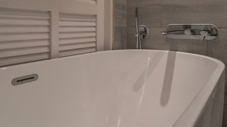 Details of the bathroom interior. A fragment of a white oval acrylic bathtub. Metal taps and a...