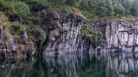 An emerald volcanic lake in an extinct crater. Steep rocky shores. Coniferous forest grows on a...