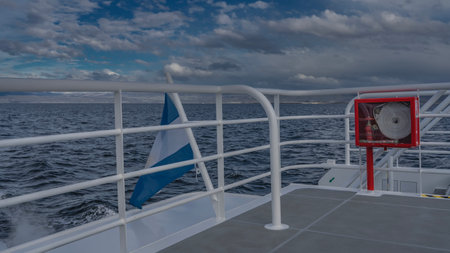 A blue-and-white cloth flutters at the stern. Ripples on the ocean surface. Clouds in the blue sky.