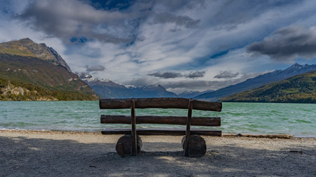 A log bench on the pebbly shore of a beautiful emerald lake. Ripples on the water. Picturesque...