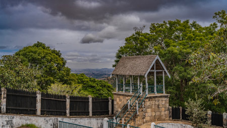A gazebo with a thatched roof, wooden railings, and a stone staircase has been built in the courtyard of the palace on the Royal Hill of Ambohimanga. Weathered board fence.の写真素材