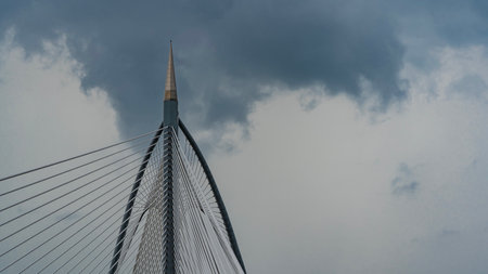 Details of the architecture of the cable-stayed bridge. A tall pillar with a spire, arches, stretched metal strings against the background of the sky and clouds. Copy space.の写真素材