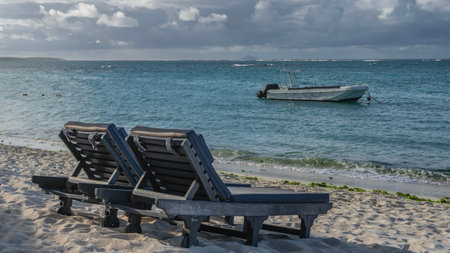 Two sun loungers with soft mattresses stand side by side on the sandy beach. The motorboat is anchored in the turquoise ocean. Blue sky, clouds. Mauritius. Belle Mare.の写真素材