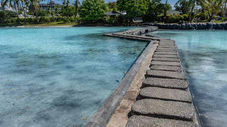 A pedestrian winding concrete path crosses a swimming pool with turquoise water. Palm trees, cottages in the distance. Philippines. Cebu.の写真素材