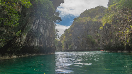 The emerald Lagoon is surrounded by inaccessible sheer karst cliffs. Green vegetation on steep...