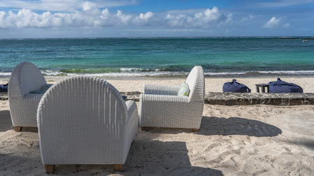 White wicker chairs with soft cushions stand on the sandy embankment. Pouf bags on the beach. The...