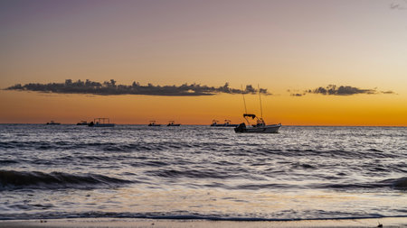 Evening after sunset. Silhouettes of anchored boats are visible in the ocean. Waves are spreading across the beach. The sky is highlighted in orange. Purple clouds. Madagascar.の写真素材