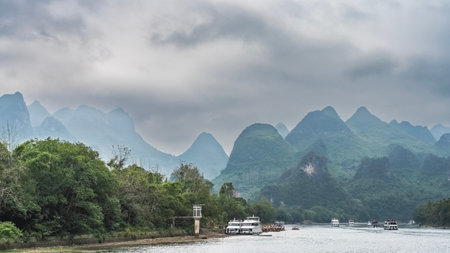 Tourist sail ships along the riverbed. The rafts are moored near the shore. Picturesque mountains against the sky. Lush green vegetation. China. Lee River. Li Jiang. Guilinの写真素材
