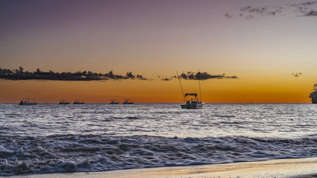 Evening after sunset. The purple sky is highlighted with orange near the horizon. The boats are anchored in the ocean. Waves are foaming on a sandy beach. Long exposure. Madagascarの写真素材