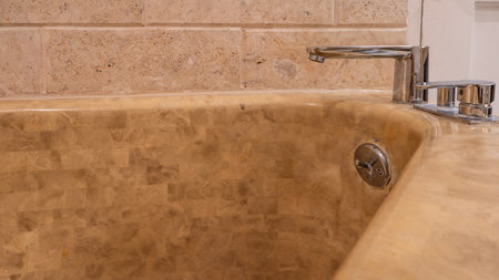 Bathroom interior details. Triangular beige bathtub against the tiled wall. A fragment. Shiny metal faucets on the edge. Close-upの写真素材