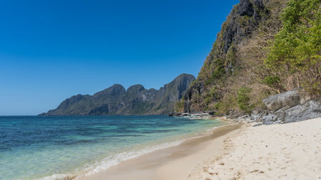 A beautiful beach on a tropical island without people. Turquoise ocean waves spread across the white sand. Boulders near the water. Green vegetation on the mountain slopes.の写真素材