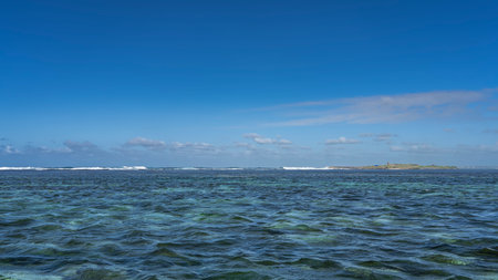 Beautiful turquoise ocean. Ripples on the surface of the water. Islet is visible in the distance, foaming waves. Blue sky, clouds. Copy space.の写真素材