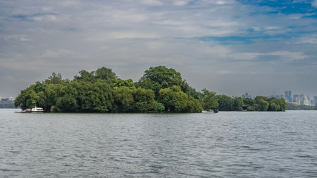 Beautiful calm lake. Tourist boats moored to the shore of the island in the middle of the reservoir. Green vegetation. Ripples on the surface of the water. City skyscrapersの写真素材