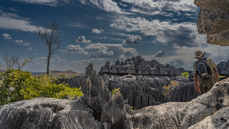The unique landscape of Madagascar. Karst rocks with sharp peaks and steep slopes. A man with backpack and climbing equipment stands on a cliff, view from the back. Blue sky, cloudの写真素材