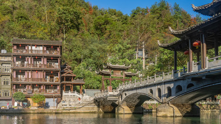 Beautiful stone arch bridge over the river. Canopies with curved roof edges, red lanterns. There are old Chinese buildings with balconies on the shore. Tourists are walkingの写真素材