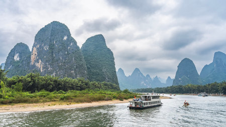 Picturesque river landscape. Tourist sail ships in the riverbed. Lush green vegetation on the shores. Beautiful mountains against the sky and clouds. China. Lijiang River Cruise.の写真素材