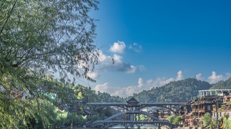 Beautiful two-tiered pedestrian bridge over the river. Stairs, red lanterns, curved roofs of canopies. Old wooden buildings on the shore. The expressway is far away. Tree branchesの写真素材