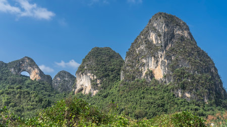 Picturesque mountains against a clear blue sky. Green vegetation on steep slopes. There is a round arched hole at the top of the cliff. China. Yangshuo. Moon Hillの写真素材