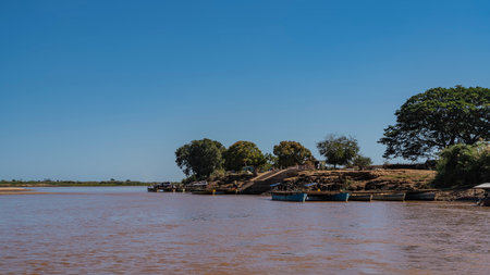 Ferry crossing. African river. Makeshift piers made of boats and wooden decking. Cars, silhouettes of people are visible. Stairs on the hillside. Clear blue sky. Green trees.の写真素材