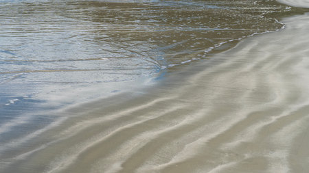 Ocean waves are spreading across the sandy beach. Close-up. Full screen. Wet wavy sand. The reflection of the sky on the shiny surface of the water. Malaysia.の写真素材
