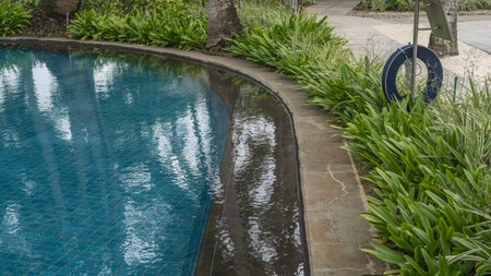 A fragment of a swimming pool. A tropical resort. The blue tiled bottom is visible through the clear water. Green vegetation along the rounded perimeter. Lifebuoy. Mauritius. Hotelの写真素材