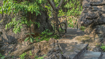 Landscaped tropical park. A boardwalk with wicker railings runs between the rocks. Lush green vegetation. Concrete stairs, steps in the foreground. China. Tianxingqiao.の写真素材