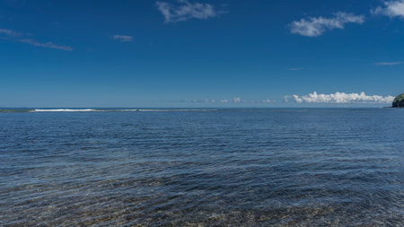 Beautiful calm seascape. Ripples on the surface of the blue ocean. The bottom is visible through the clear water. Foam waves in the distance. Azure sky, white clouds. Copy space.の写真素材