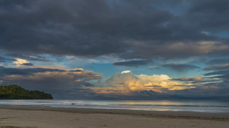 Sunset on a tropical island. The clouds in the blue evening sky are highlighted in gold and pink. Ocean waves are spreading across the sandy beach. Reflection on the sea surface.の写真素材