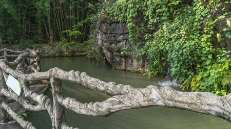 Walking path along the pond. A handrail woven from branches in the foreground. Green vegetation on steep cliffs. Bamboo thickets in the distance. China.Heavenly Star Bridge Park.の写真素材