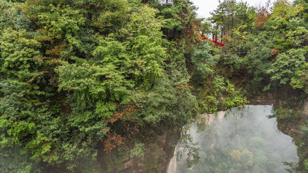 A natural stone bridge between the rocks. The arch over the gorge. There is green vegetation on the steep slopes of the mountains. Red ribbons on the railing of the footpath. Fog.の写真素材