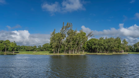 Golf course. Golf cart on a green manicured lawn, trees against a background of blue sky and clouds. There is a lake in the foreground. Mauritius.の写真素材