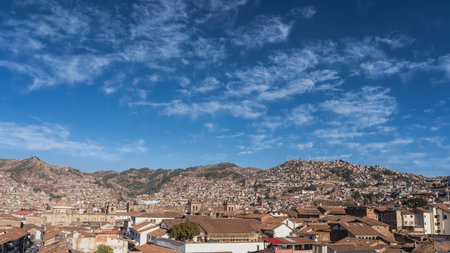 Panorama of the Cuzco city. View from the height. There are many closely built buildings with red tiled roofs. The towers of the Catholic Cathedral are visible. Mountainsの写真素材
