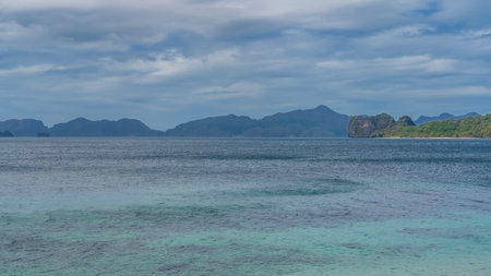 Beautiful seascape. Calm turquoise ocean, blue sky, clouds. Green vegetation on the hill. Mountains...