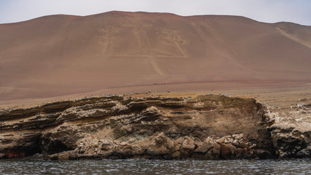 An ancient mysterious Paracas Candelabra drawing on the slope of a sandy hill. A geoglyph in the shape of a trident. The ocean, the rocky shore in the foreground. Peru. Pisco Bayの写真素材