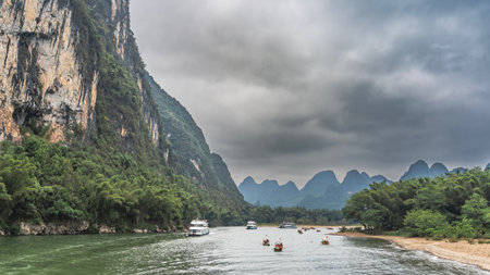 Tourist and ships bamboo rafts float along the picturesque river. The riverbed bends. There is green vegetation on the shores. Mountains against the sky and clouds. China. Lee Riverの写真素材