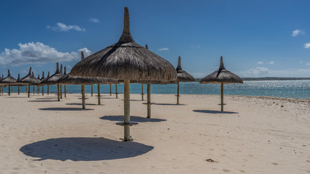 Rows of straw umbrellas on a sandy beach without people. Round shadows on white sand. A calm turquoise ocean. Blue sky, clouds. low season. Mauritiusの写真素材