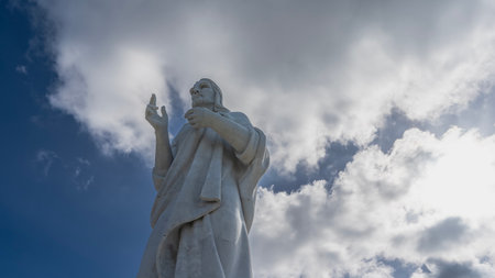 A huge statue of Christ against a background of blue sky and clouds. Sculpture made of white Carrara marble. Bottom-up view. Cuba. Havana. Jesus of Nazarethの写真素材